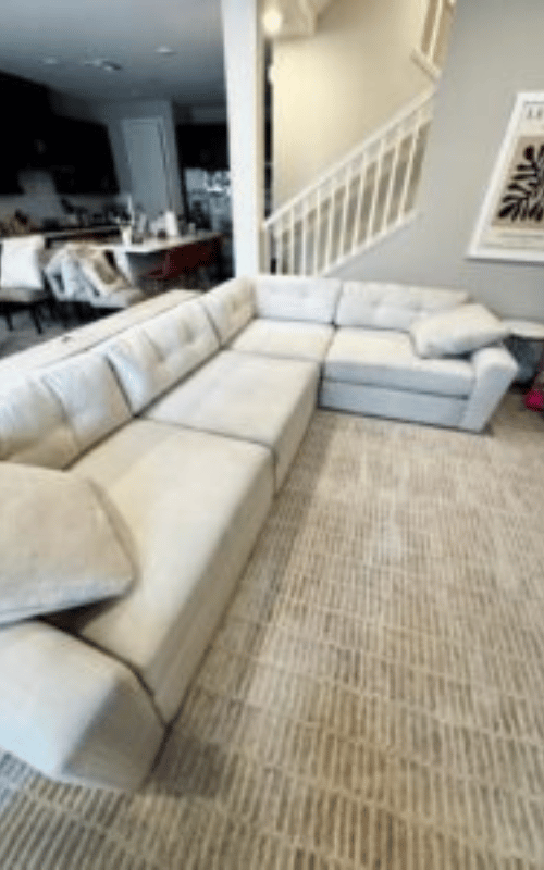 A uniformed technician wearing blue protective shoe covers uses a steam wand to clean a grey carpet, revealing a visible contrast between the clean and dirty sections. This demonstrates the effectiveness of professional stain removal in Los Gatos.
