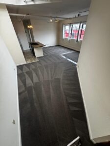 High-angle view of a loft apartment with large windows and clean grey carpeting. The uniform cleaning pattern covers the entire living surface, highlighting our ability to handle large cleaning projects in San Jose.